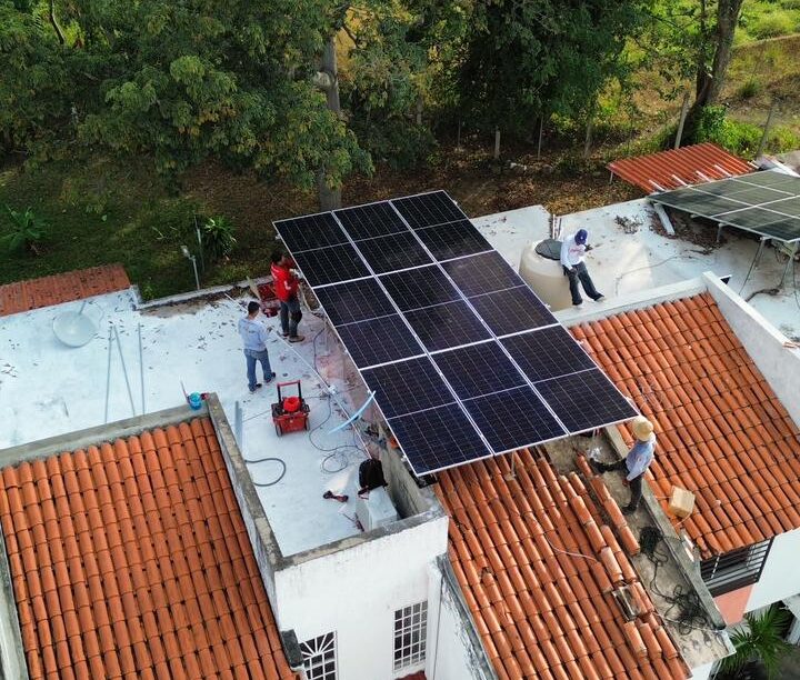 Instalación de nueve paneles solares bifaciales en la azotea de una vivienda en Prados de la Montaña, San Esteban, Puerto Vallarta, con técnicos trabajando sobre la estructura Aluminext y vista aérea del entorno arbolado